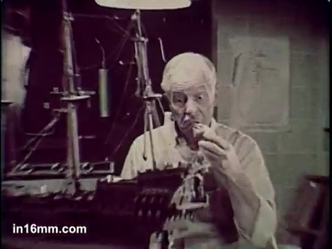 The still from the 'Total Cereal Commercial' features an older man examining a small object in his hand while standing in front of a detailed ship model. The setting appears to be a workshop or studio, with drawings and tools in the background, suggesting a creative or crafting environment. The overall tone is nostalgic and focused on the man's contemplative expression, highlighting his attention to detail.