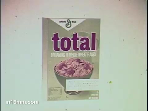 The still features a box of General Mills' 'Total' cereal, prominently displaying the brand name 'total' in bold purple letters. The packaging emphasizes it contains '8 vitamins in whole wheat flakes' alongside a bowl of the cereal, showcasing its texture. The overall design is vibrant and aimed at attracting health-conscious consumers.