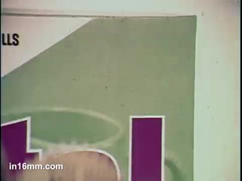 The still features a close-up of a cereal box, likely depicting 'Total' cereal. The design includes bold, colorful text, predominantly purple, set against a light green background. The focus on the packaging emphasizes the product’s branding, suggesting a promotional context typical of television commercials.