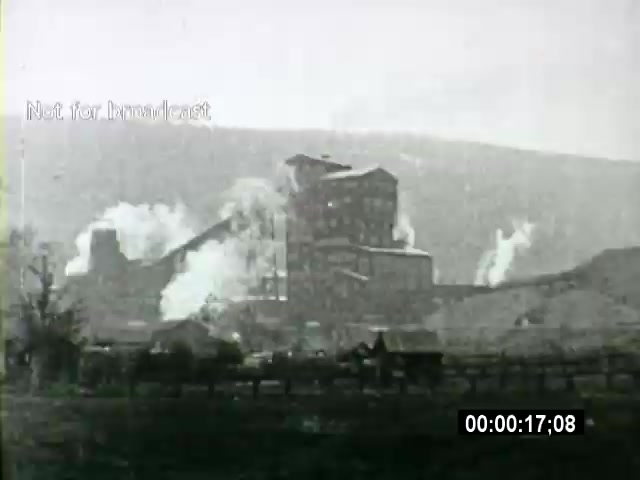 The still from the 'John L Lewis 1919 Miner Strike footage' depicts a coal processing facility, prominently featuring smokestacks emitting clouds of smoke against a distant, hilly backdrop. The image reflects the industrial landscape of the time, illustrating the heavy machinery and labor involved in coal mining. The black-and-white tone emphasizes the historical context of the early 20th-century labor struggles. The caption 'Not for broadcast' indicates this footage is likely intended for archival or educational purposes.