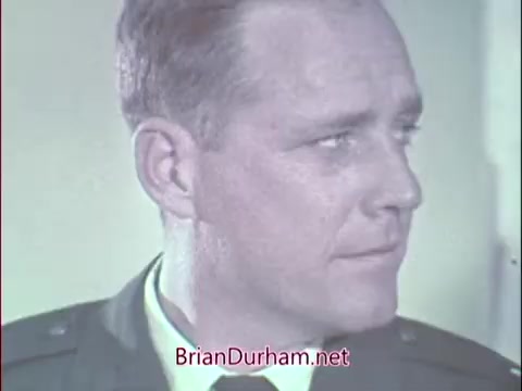 The still features a man in an Air Force uniform, likely a doctor or recruiter, with a serious expression. His profile suggests he is engaged in conversation or thought, conveying professionalism aligned with the military context. The background appears neutral, emphasizing his focused demeanor. This image captures a moment from a Vietnam-era recruitment commercial targeting medical professionals for the Air Force Reserve.