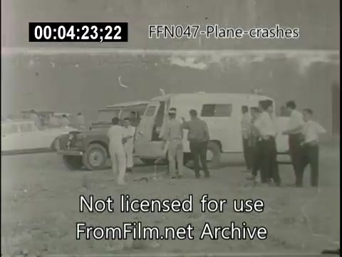 The still depicts a scene at the site of a plane crash, featuring a group of individuals gathered around vehicles, including a van and several cars. The people appear to be engaged in discussions or assessments related to the incident. The image is in black and white, typical of historical newsreel footage. The timestamp suggests it is part of a longer segment within the footage titled 'FFN047-Plane-crashes.'