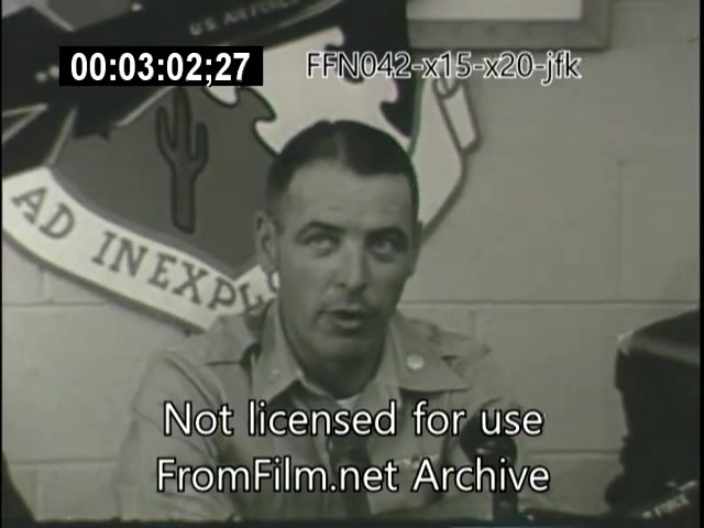 The still features a man in uniform speaking during a press or official conference, likely related to aerospace projects like the X-15 or X-20 Dynasoar. Behind him, there is an emblem or insignia that includes a cactus and the phrase 'AD INEXPLORED.' The footage timestamp indicates it is part of a documentary or archival presentation. The context suggests a discussion on significant aerospace developments during the era, possibly linked to the Kennedy administration.