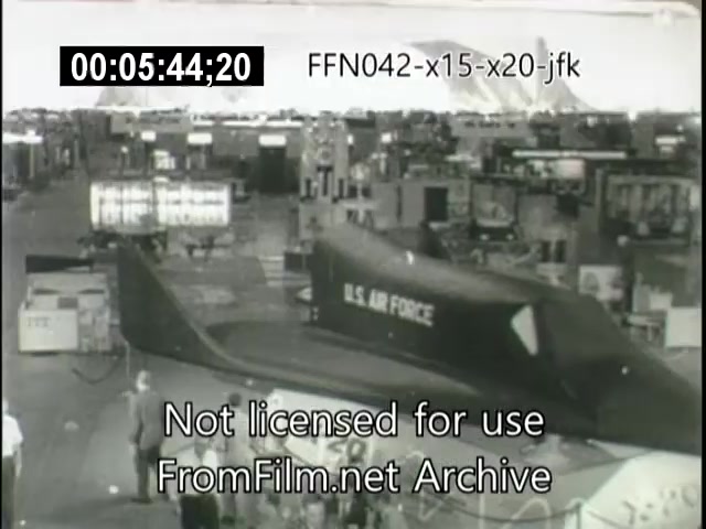 The still features a vintage black-and-white film clip showcasing various exhibits, prominently displaying a model or mockup of the X-20 Dynasoar spacecraft. The setting appears to be an exhibition or event space filled with other displayed items in the background. The U.S. Air Force insignia is visible on the Dynasoar model, emphasizing its military significance. The timestamp indicates the moment within the footage, and a watermark notes the image's licensing status.