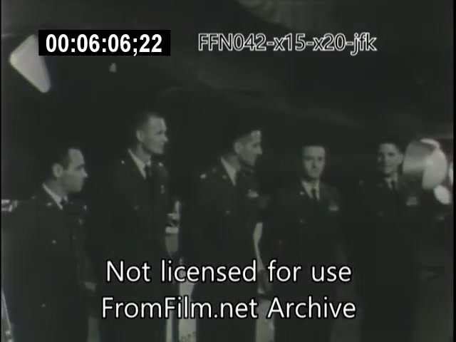 The still captures a group of individuals, likely military personnel or astronauts, standing together, possibly in a ceremonial or formal setting related to aviation or space exploration. They are dressed in uniforms, indicating a professional context. The background suggests a space or aviation facility, aligning with the themes of the X-15 and X-20 Dynasoar programs, as well as the historical significance of figures like JFK in aerospace advancements. The overlay text indicates the footage is not licensed for use and is archived material.