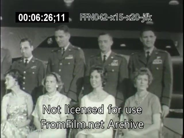 The still features a group of six men in military uniforms and five women in dresses, seated in a posed arrangement. The backdrop suggests a formal event related to aerospace, possibly commemorating achievements like the X-15 or X-20 Dynasoar programs, and the inclusion of JFK indicates a high-profile occasion. The overall ambiance is ceremonial, reflecting an important moment in aviation history.