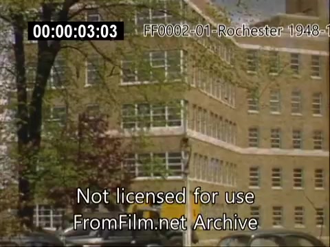 The still depicts a building associated with the University of Rochester's School of Medicine, captured in 16mm Kodachrome film from 1948-1950. The architecture features a modern design typical of mid-20th century educational institutions, with large windows and a light-colored façade. Surrounding trees suggest a campus setting, adding to the scholarly atmosphere of the time. The footage reflects the historical context of the university during that period.