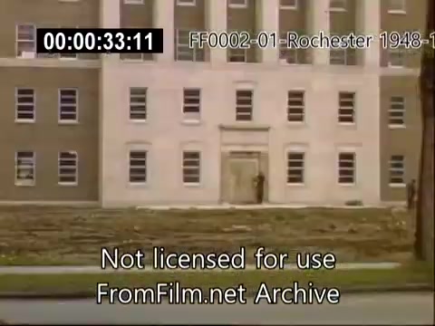 The still features a building associated with the Rochester School of Medicine, captured in Kodachrome film from approximately 1948-1950. The facade shows a prominent entrance with large windows, typical of mid-century architecture. The foreground is devoid of vegetation, suggesting ongoing landscaping or development. The overall scene reflects the academic environment of the University of Rochester during this period.