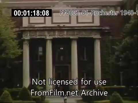 The still depicts a building associated with the University of Rochester, likely from the Rochester School of Medicine, featuring classical architecture with prominent columns. The exterior is framed by neatly trimmed greenery, and the image reflects the aesthetic of the late 1940s to early 1950s, showcasing the historical character of the university during that period.