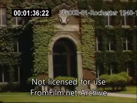 The still features the entrance of a historic building at the University of Rochester, likely from the Rochester School of Medicine. The façade is adorned with ivy, typical of mid-20th century collegiate architecture. The scene captures a moment from home movies taken between 1948 and 1950, showcasing the university's environment during that era. The overall tone reflects a nostalgic glimpse into the campus life of the time.