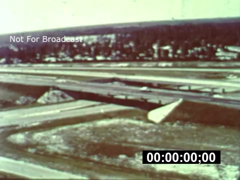 The 16mm still from 'WDW preview - from when the park was under construction' shows an aerial view of a construction site. It features expansive cleared land with dirt mounds and unpaved roads. The landscape is largely rural, with trees lining the horizon, indicating the area is in the early stages of development for Walt Disney World. The image captures a sense of anticipation for the future park, highlighting the scale of the project during its initial phases.