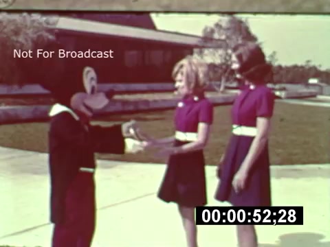 The still from the 16mm print shows Mickey Mouse interacting with two young women dressed in matching purple dresses with white belts. The background appears to feature a partially constructed building, indicative of the early stages of Walt Disney World. The scene evokes a sense of nostalgia and excitement for the park's future. A timestamp at the bottom suggests it is part of a larger preview film.