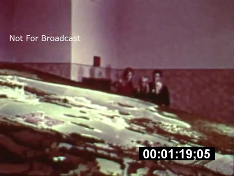 The still from the 16mm print shows a group of individuals, likely visitors, standing in front of a large model or blueprint representing the layout of Walt Disney World during its construction phase. The scene gives a glimpse into the early conceptualization of the park, highlighting the intricate details of the planned attractions and areas. The colors and quality reflect the vintage feel of the film, marking a significant moment in Disney history. Prominent text indicates that this material is not for broadcast.