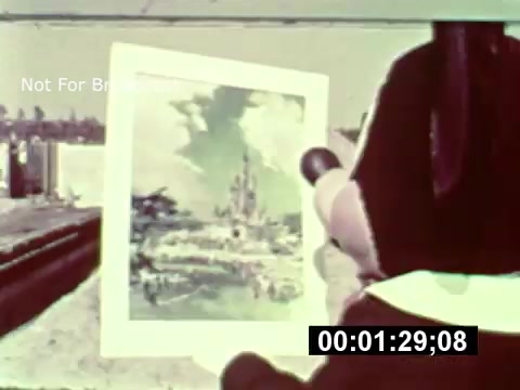 The still from the 16mm print of 'WDW Preview' features a character holding up an illustrated concept of the park, showcasing a vibrant landscape with a castle in the background. The image captures a moment from the park's construction phase, highlighting the anticipation and excitement around the development of Walt Disney World. The colorful illustration contrasts with the unfinished surroundings, emphasizing the vision for the future park.