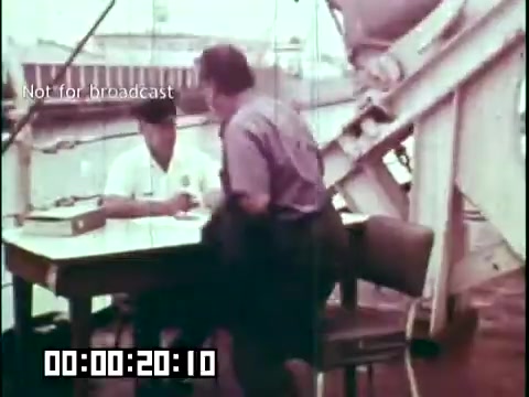 The still from 'Immigrant Heritage' features a scene on a ship, likely during the mid-20th century. It shows a man, dressed casually, interacting with a uniformed official at a table. The setting suggests a checkpoint or immigration processing area, reflecting the themes of the film which explores Irish immigrant experiences. The film is marked as 'Not for broadcast,' indicating it may be for internal or educational use.