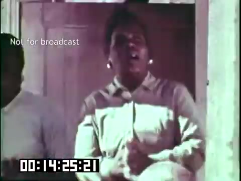 The still from the film 'Immigrant Heritage' features a person passionately singing or speaking, likely in a cultural context. They appear engaged and expressive, contributing to the educational theme of the film. The setting seems informal, possibly a gathering or performance space. A timestamp indicating a specific point in the film is also visible, noting that the clip is not intended for broadcast.