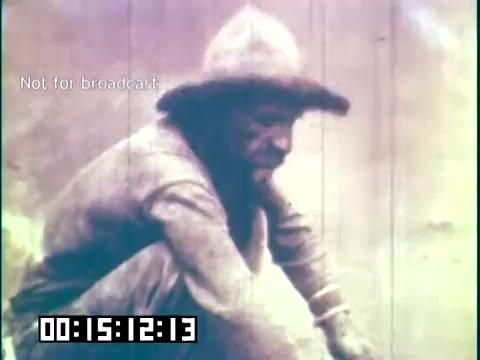 The still from 'Immigrant Heritage' features a man in a wide-brimmed hat, seated and engaged in an activity. His expression appears contemplative, and the scene is rendered in a muted color palette typical of historical footage. The context suggests a focus on immigrant experiences, with the Irish Rovers likely providing a cultural connection through music or storytelling. The timestamp indicates it is part of a longer film segment, denoted as not for broadcast.