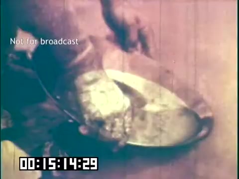 The still from 'Immigrant Heritage' features a close-up of a hand handling a metallic bowl or dish. The image has a warm, vintage hue, typical of 16mm film, giving it an endearing, nostalgic feel. The context suggests a focus on cultural practices or traditions, likely within an immigrant narrative. The time stamp indicates that this is part of a specific sequence in the film. The 'Not for broadcast' label indicates the still is not meant for public airing.