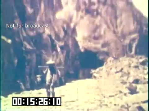 The still from 'Immigrant Heritage' features a figure walking along a rocky path, carrying a load on a stick, suggesting themes of labor and resilience often associated with immigrant experiences. The background shows rugged terrain, possibly signifying the challenges faced by immigrants. The timestamp indicates it is from the film's middle section, while the text 'Not for broadcast' suggests it is for internal or educational use only. The overall tone of the image reflects the historical and cultural journey of immigrants.