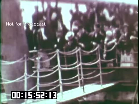 The still captures a group of passengers on a ship's deck, likely during the early 20th century. They appear to be preparing to disembark, with ropes visible in the foreground and a crowd in the background. The scene conveys a moment of anticipation and transition, reflecting the immigrant experience as depicted in the educational film 'Immigrant Heritage' featuring the Irish Rovers. The color is muted, typical of 16mm film, enhancing the historical context.