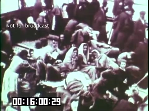 The 16mm still from 'Immigrant Heritage' captures a crowded scene, likely aboard a ship, depicting many individuals, some wrapped in blankets, appearing weary and reflective. The atmosphere conveys the struggles and resilience of immigrants, emphasizing their journey towards a new life. The vintage quality of the film adds historical context to these poignant moments.
