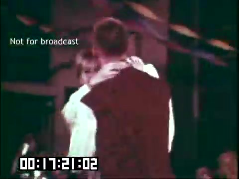 The still from 'Immigrant Heritage' features two individuals dancing intimately, possibly expressing cultural connection through movement. The background suggests a festive atmosphere, likely during a celebration. The scene captures a moment of connection, reflecting themes of heritage and community. A timecode indicates it's part of a larger film segment.