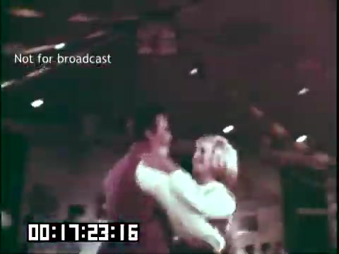 The still from 'Immigrant Heritage' features a couple dancing closely, likely in a lively setting that reflects cultural celebration. The warm lighting and soft focus suggest a nostalgic atmosphere, typical of educational films aimed at showcasing immigrant traditions. The timestamp and 'Not for broadcast' label indicate it's part of a larger, possibly archival, production.