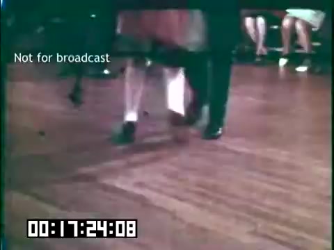 The still from 'Immigrant Heritage' features a dance scene, likely showcasing traditional Irish dance, with performers displaying energetic footwork. The focus is on the dancers' legs and feet, highlighting their movements against a wooden floor. In the background, seated audience members are partially visible. The frame is marked 'Not for broadcast,' indicating its archival nature. The overall atmosphere reflects a celebration of cultural heritage through dance.