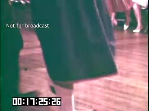 The still features a close-up shot focusing on the lower half of a person dressed in a costume, likely representing traditional Irish attire. The setting appears to be a lively cultural or community event, with wooden flooring visible in the background. Other participants, wearing various dresses, can be seen slightly blurred, hinting at a festive atmosphere. The title 'Not for broadcast' indicates this is a behind-the-scenes or unreleased portion of the educational film showcasing immigrant heritage through dance and music.