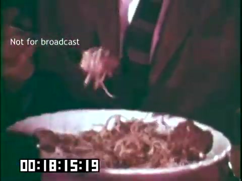 The still shows a close-up of a person holding a fork with spaghetti, indicating a meal being served or enjoyed. The setting appears informal, likely reflecting cultural traditions or immigrant experiences associated with food. The text overlay states 'Not for broadcast,' and a timestamp is displayed at the bottom. The context is related to the educational film 'Immigrant Heritage,' featuring the Irish Rovers, which likely explores themes of heritage and community.