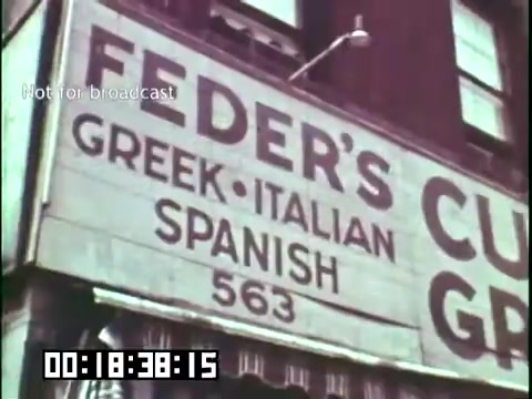The still features a sign for 'Feder's,' which advertises Greek, Italian, and Spanish cuisine. The text indicates the establishment's address as 563. The image's educational context, associated with the 'Immigrant Heritage' film featuring the Irish Rovers, likely highlights the cultural diversity and contributions of immigrant communities. The timestamp suggests a specific moment within the film, emphasizing the significance of these culinary influences.