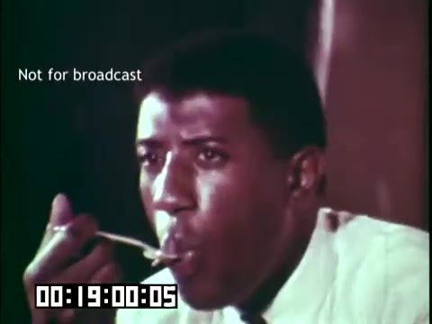 The still from the educational film 'Immigrant Heritage' featuring the Irish Rovers shows a young man, who appears to be eating or tasting something, with a spoon in hand. His expression suggests focus or contemplation. The scene emphasizes personal experience, possibly related to immigrant culture. The text 'Not for broadcast' indicates it's not intended for public viewing. The timecode shows the moment is from 19 seconds into the film.