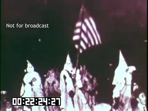 The still from 'Immigrant Heritage' features a group of individuals dressed in white robes, associated with the Ku Klux Klan, carrying an American flag. The context suggests a discussion surrounding immigrant heritage and identity, potentially highlighting historical tensions or conflicts related to immigration in America. The 'Not for broadcast' label indicates it's intended for educational or archival purposes.