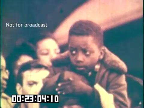 The still from the educational film 'Immigrant Heritage' featuring the Irish Rovers captures a moment of emotional significance. It shows a young child, with a concerned expression, seated atop another person's shoulders amidst a crowd. The background hints at a larger gathering, likely related to themes of immigration and community. The image highlights the poignant experiences of immigrants, emphasizing themes of hope and resilience. The text indicates that it is not for broadcast, suggesting it is a part of a larger documentary or educational narrative.