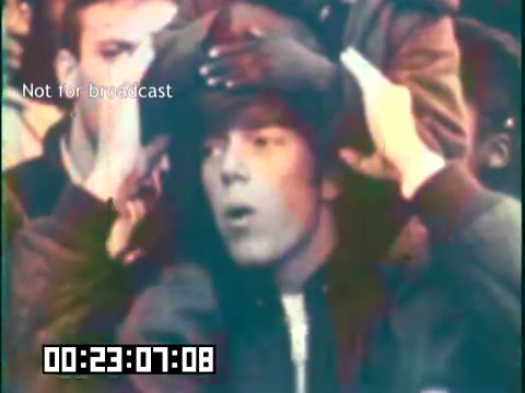 The still depicts a young man with a focused expression, surrounded by a group in a vibrant setting. People appear engaged, likely in a moment of audience participation during the educational film featuring the Irish Rovers. The scene captures a lively atmosphere, emphasizing the theme of community and cultural heritage. A timecode and a 'not for broadcast' label are visible, indicating it's part of a film edit.