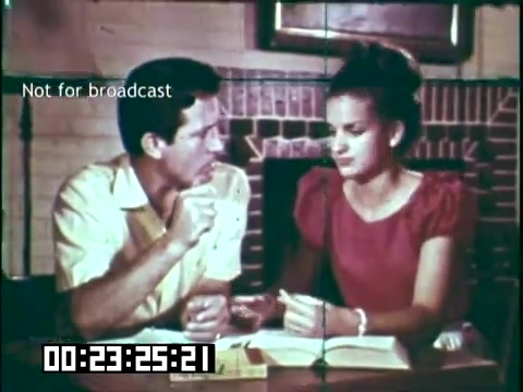 The still features two individuals engaged in a conversation at a table. The male, wearing a light-colored shirt, appears animated as he gestures, while the female, dressed in a red blouse, listens intently. The setting has a rustic feel, with a brick fireplace in the background. The text 'Not for broadcast' suggests it's a private or behind-the-scenes moment from the educational film 'Immigrant Heritage,' which highlights the contributions of various immigrant communities, particularly focusing on the Irish.