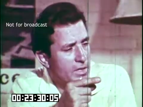 The still from 'Immigrant Heritage' features a man engaged in a discussion, emphasizing a point with his finger while appearing thoughtful. The surrounding context suggests an educational focus on cultural heritage. The timestamp at the bottom indicates it is part of a longer film, while a label notes it's not for broadcast, implying it may be used for archival or educational purposes.