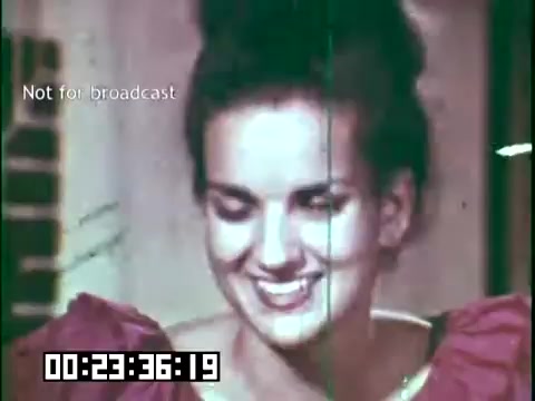 The still from 'Immigrant Heritage,' featuring the Irish Rovers, shows a young woman smiling warmly. She appears engaged and cheerful, wearing a vibrant outfit with puffed sleeves, suggestive of a historical or cultural theme. The film has a vintage aesthetic, characterized by grain and a slight color overlay, indicating it was shot on 16mm film. The scene captures a moment of joy and connection, likely reflecting themes of cultural heritage and community in the context of the film. A timestamp and text indicating 'Not for broadcast' are visible at the bottom.