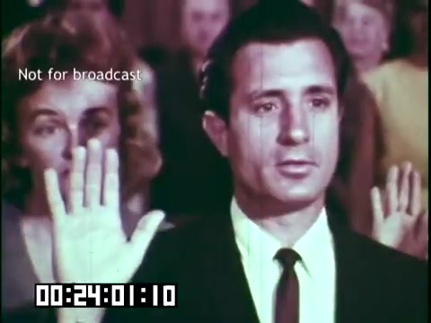 The still from 'Immigrant Heritage,' features a man in a suit raising his right hand, likely in a gesture of affirmation or oath. In the background, a woman appears to be raising her hand as well. The scene suggests a moment of significance, possibly related to citizenship or community involvement. The coloring and film quality indicate it was shot in the mid-20th century. The text 'Not for broadcast' suggests this is a behind-the-scenes or archival image.
