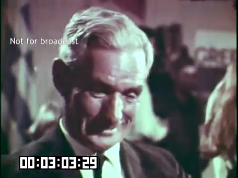 The still from 'Immigrant Heritage' features a man with gray hair and a friendly demeanor, smiling warmly at the camera. The setting appears to be a gathering or event, possibly celebrating cultural heritage, with indistinct figures and flags in the background. A timestamp indicating 3 minutes and 29 seconds is visible at the bottom. The image includes a watermark stating 'Not for broadcast,' indicating it is intended for internal use or archival purposes.