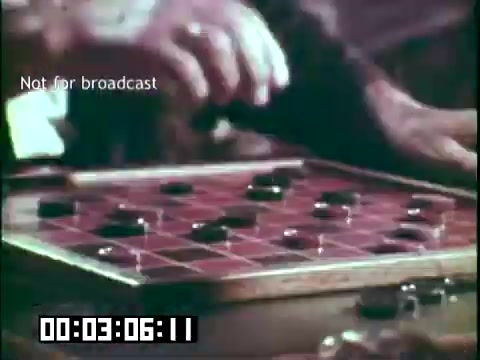 The still from 'Immigrant Heritage' features a close-up of a wooden checkers board. A hand is in motion, likely making a move with one of the game pieces. The image conveys a sense of nostalgia and community, emphasizing the cultural aspects of play and interaction. The timestamp indicates it's from a segment about 3 minutes into the film, and there's a label stating 'Not for broadcast.'