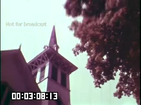 The still features a church steeple surrounded by trees, set against a clear sky. The focus is on the architectural details of the steeple, which has a prominent peak, indicating a traditional design. The image has a vintage hue characteristic of 16mm film, contributing to its educational documentary feel. The text 'Not for broadcast' appears, suggesting it's a production still not intended for public distribution.