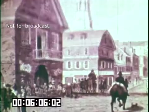 The still from 'Immigrant Heritage' features a historical scene depicting a bustling street with crowds gathered outside buildings, indicative of an earlier era, possibly related to Irish immigration. The foreground shows a horseman, while the architecture suggests a quaint historical setting. The overall tone hints at themes of community and heritage. The frame includes a timestamp and a note indicating that it is not for broadcast.