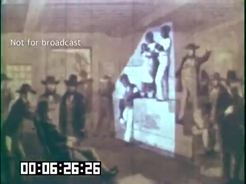 The still from 'Immigrant Heritage' features a historical reenactment scene where a diverse group of people, possibly immigrants, are gathered in a room. They appear engaged in a performance or presentation, with some individuals standing on a platform. The backdrop includes projected images, enhancing the educational theme of the film. The setting captures the spirit of community and cultural heritage among immigrants, conveyed through visual storytelling. A timestamp indicates the moment in the film, and a note specifies it is not for broadcast.