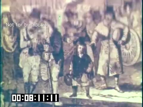 The still from 'Immigrant Heritage' - an educational film featuring the Irish Rovers - depicts a historical scene involving a group of immigrants. Notable elements include diverse clothing styles that reflect the cultural background of the figures, with a focus on a child at the forefront. This imagery likely aims to convey themes of heritage, struggle, and community among immigrants. The film emphasizes the importance of recognizing and preserving cultural identities.