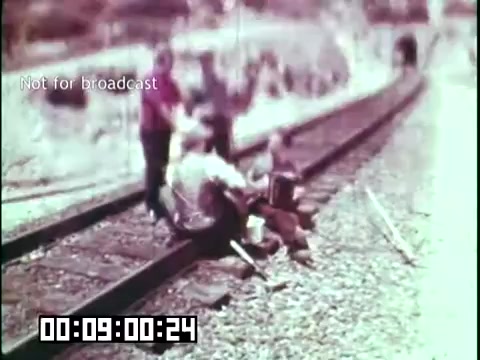 The still from 'Immigrant Heritage' features a group of people sitting on a railway track, most likely engaged in a discussion or recreation. The visual tone suggests a nostalgic or historical context, typical of educational films. The scene is informal and captures a moment of cultural exchange, reflecting the themes of immigration and heritage. The image is marked 'Not for broadcast,' indicating that it is intended for archival or educational purposes rather than commercial distribution.