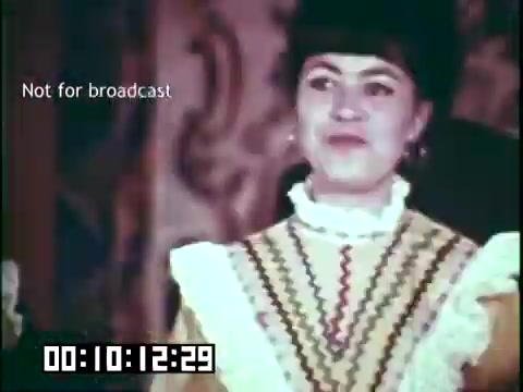 The still features a woman in traditional attire, possibly reflecting a cultural heritage theme relevant to the 'Immigrant Heritage' film. Her outfit includes intricate patterns and frills, indicative of historical costume styles. The background suggests a festive or cultural setting, aligning with the educational focus on immigrant heritage. The text 'Not for broadcast' and the timecode at the bottom indicate that this is a still from a film reel.