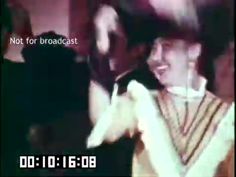 The still from 'Immigrant Heritage' features a joyous scene involving celebration and cultural expression. A performer, possibly dressed in traditional attire, dances enthusiastically, contributing to the vibrant atmosphere. The presence of people in the background suggests a lively gathering, emphasizing themes of community and heritage related to Irish culture. The timestamp indicates a specific moment in the film, capturing the essence of the celebration.