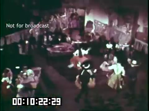 The still depicts a lively scene from the educational film 'Immigrant Heritage,' featuring the Irish Rovers. In a colorful indoor setting, people dressed in traditional attire are dancing and socializing, capturing the festive spirit of Irish culture. The background suggests a celebration, with decorative elements enhancing the atmosphere. The image is marked with the text 'Not for broadcast,' indicating it is a still from a private or archival source.