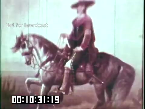 The still from 'Immigrant Heritage,' an educational film featuring the Irish Rovers, depicts a mounted figure dressed in period attire. The figure appears to be a historical representation, possibly conveying themes related to Irish heritage or history. The background is minimalistic, emphasizing the rider and horse. The image has a vintage aesthetic, characteristic of 16mm film, reflecting a historical context. The timecode indicates a specific point in the film, suggesting that this scene may play a significant role in the narrative.